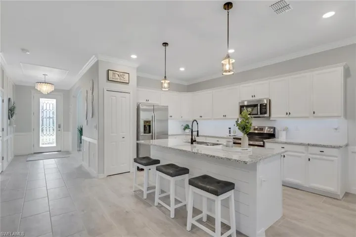 Kitchen featuring white cabinets, a kitchen breakfast bar, light stone counters, stainless steel appliances, and a kitchen island with sink