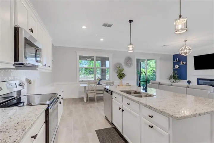 Kitchen featuring stainless steel appliances, white cabinetry, light stone countertops, an island with sink, and crown molding