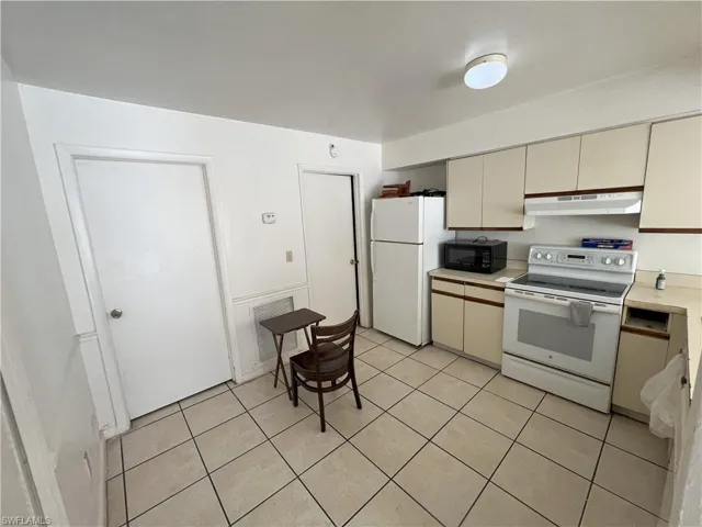 Kitchen with cream cabinets, light tile patterned floors, and white appliances