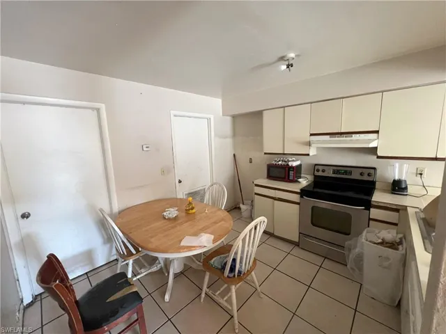 Kitchen with light tile patterned flooring, stainless steel electric range oven, and cream cabinets