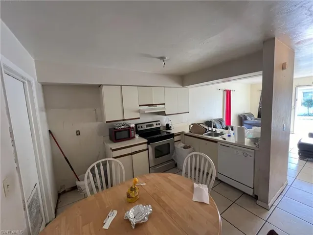 Kitchen with stainless steel electric stove, dishwasher, white cabinets, and light tile patterned floors