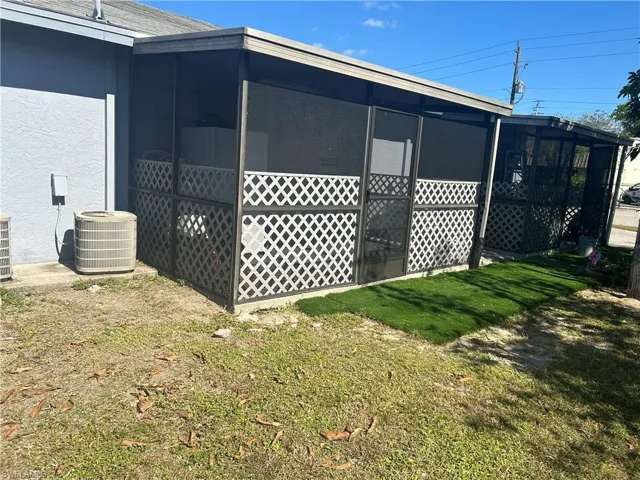 View of side of property featuring a sunroom, central air condition unit, and a lawn