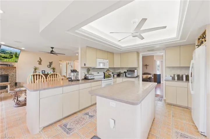 Kitchen with cream cabinetry, a peninsula, a ceiling fan, white appliances, and a kitchen island