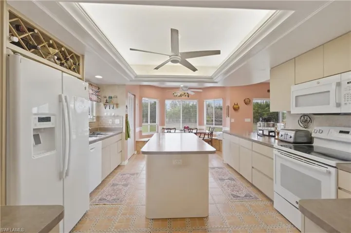 Kitchen featuring white appliances, a kitchen island, cream cabinetry, crown molding, and light countertops