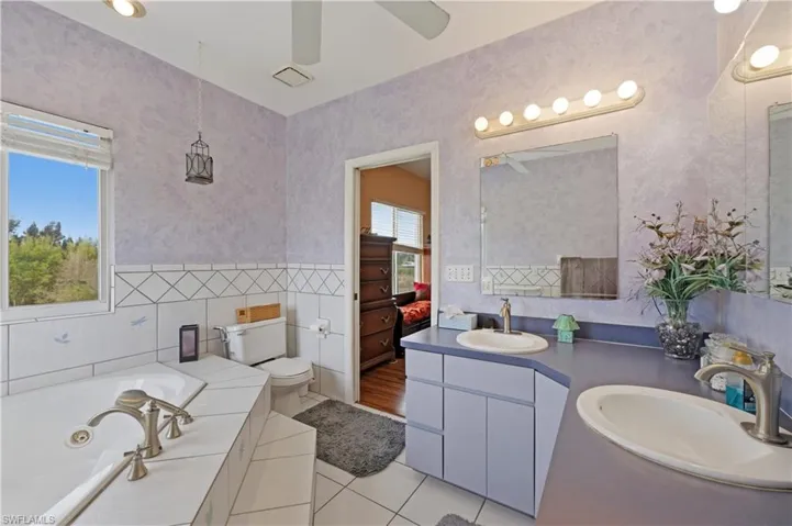 Bathroom featuring double vanity, light tile patterned floors, a jetted tub, ensuite bath, and tile walls