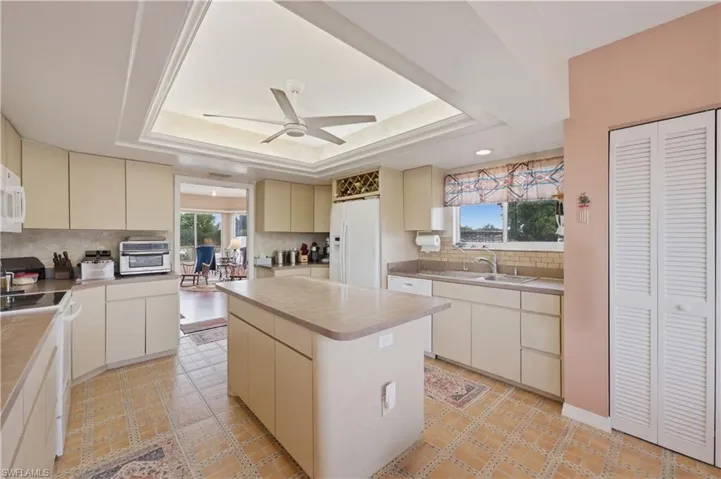 Kitchen featuring cream cabinets, a kitchen island, ceiling fan, white appliances, and tasteful backsplash