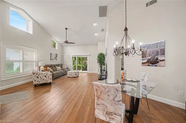 Vaulted ceilings with a ceiling fan, hardwood flooring, a glass-top dining table with a wrought iron chandelier, and white window shutters