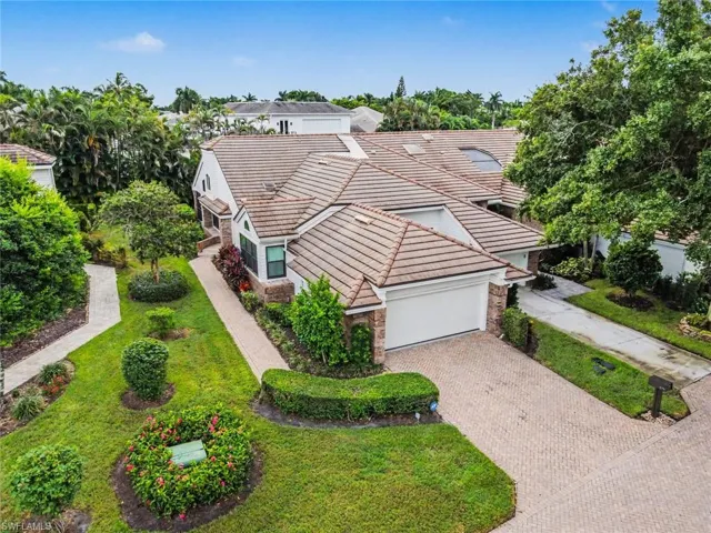 Paved driveway leading to an integrated garage, brick-accented exterior with a tiled roof, and established landscaping with mature trees