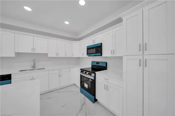 Kitchen featuring white cabinetry, light-toned countertops, a stainless-steel sink with a gooseneck faucet, a blue and black range, and a matching blue and black microwave