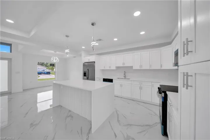 White shaker cabinetry, recessed lighting, and a kitchen island with fluted paneling