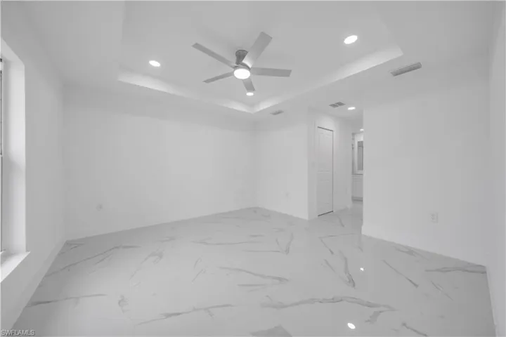 Recessed lighting, ceiling fan, tray ceiling, tile flooring, and a window providing natural light