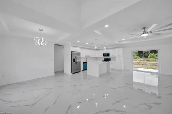 Spacious open-concept living area with white tile flooring, vaulted ceilings, and recessed lighting