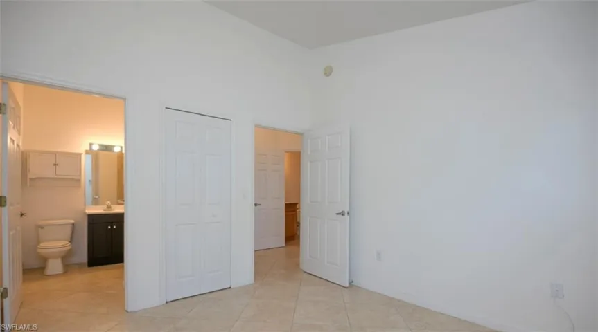 Unfurnished bedroom featuring connected bathroom, light tile patterned floors, a high ceiling, a closet, and a sink