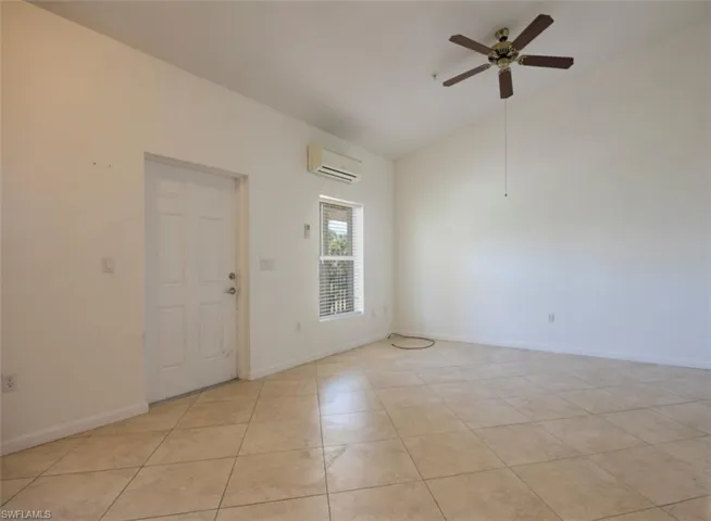 Unfurnished room featuring light tile patterned floors, baseboards, ceiling fan, an AC wall unit, and vaulted ceiling