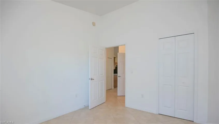 Unfurnished bedroom featuring light tile patterned floors, a closet, baseboards, and a high ceiling