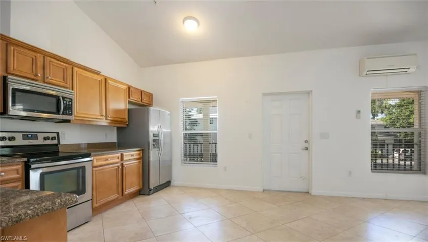 Kitchen with a wall mounted air conditioner, lofted ceiling, appliances with stainless steel finishes, and brown cabinets
