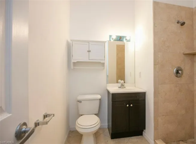 Bathroom featuring baseboards, toilet, a tile shower, tile patterned floors, and vanity