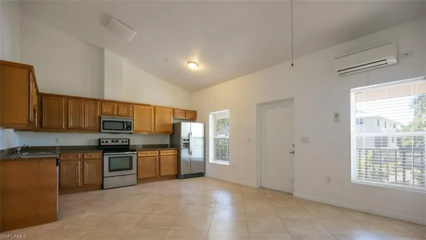 Kitchen with a wall unit AC, baseboards, stainless steel appliances, dark countertops, and brown cabinets
