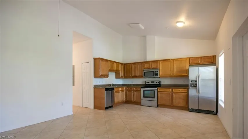 Kitchen featuring high vaulted ceiling, light tile patterned flooring, stainless steel appliances, dark countertops, and brown cabinets