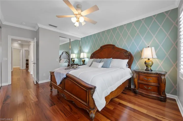 Bedroom with wallpapered walls, ornamental molding, dark wood-type flooring, an accent wall, and a ceiling fan