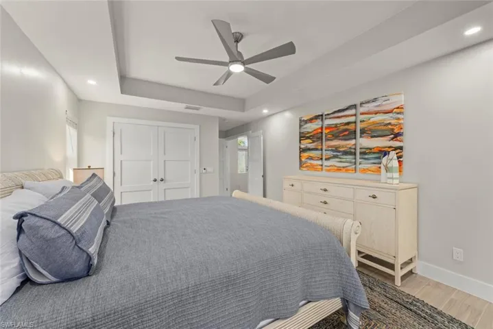 Bedroom with recessed lighting, ceiling fan, a tray ceiling, a closet, and light wood-style flooring