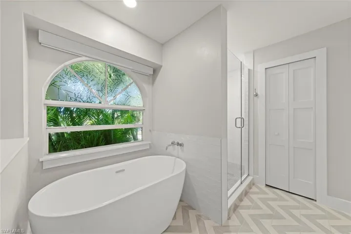 Full bathroom with a freestanding tub, a shower stall, light floors, and a closet