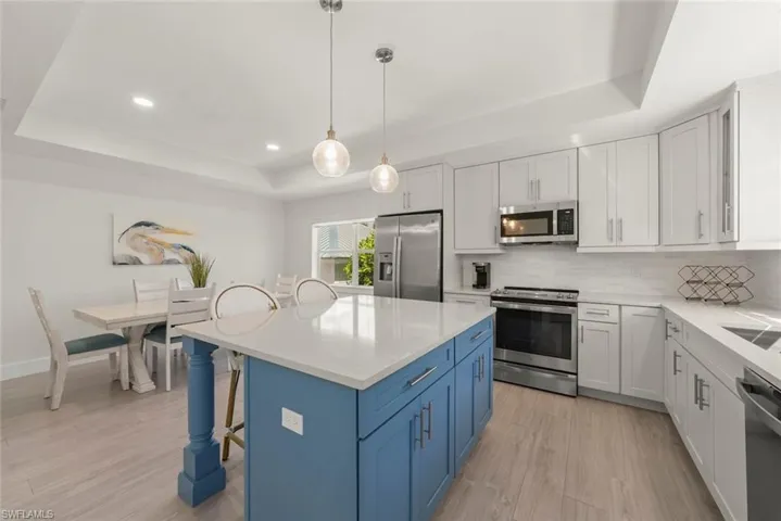 Kitchen featuring a tray ceiling, two tone cabinets, a breakfast bar, stainless steel appliances, and a center island