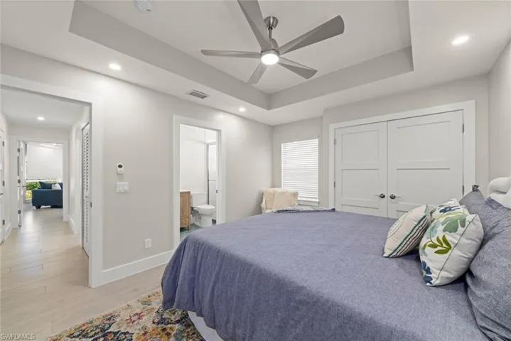 Bedroom featuring recessed lighting, light wood finished floors, a raised ceiling, a ceiling fan, and ensuite bathroom