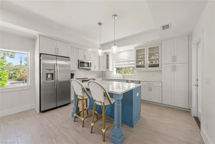 Two tone kitchen with stainless steel appliances, hanging light fixtures, glass fronted cabinets, light wood-style floors, and a breakfast bar area