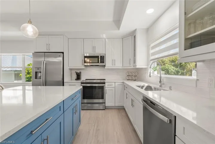 Kitchen featuring stainless steel appliances, dual tone cabinetry, light stone countertops, pendant lighting, and light wood-style flooring