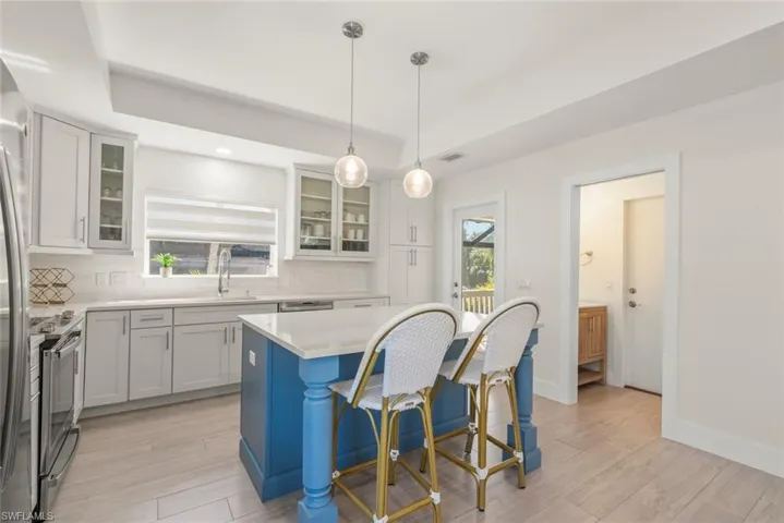 Kitchen with light wood-style floors, stainless steel appliances, a breakfast bar area, glass fronted cabinets, and a tray ceiling