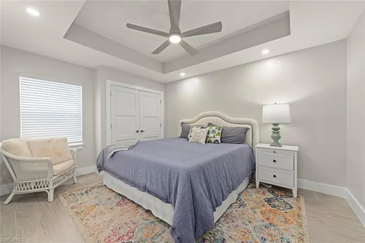 Bedroom featuring a tray ceiling, light wood-type flooring, ceiling fan, a closet, and recessed lighting