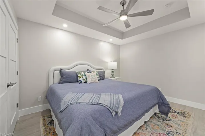Bedroom with a raised ceiling, a closet, light wood-style flooring, ceiling fan, and recessed lighting
