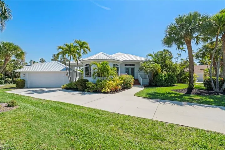 Single story home with a front yard, driveway, a garage, and a metal roof