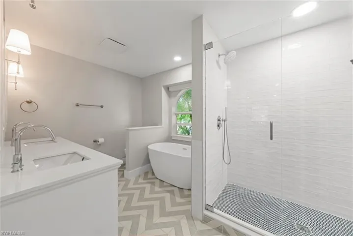 Bathroom featuring double vanity, a stall shower, a freestanding bath, light floors, and recessed lighting
