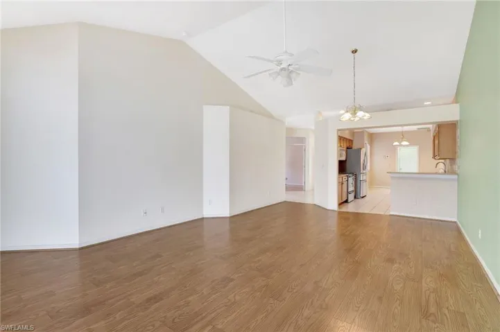 Unfurnished living room with light wood-type flooring, high vaulted ceiling, ceiling fan with notable chandelier, baseboards, and a sink