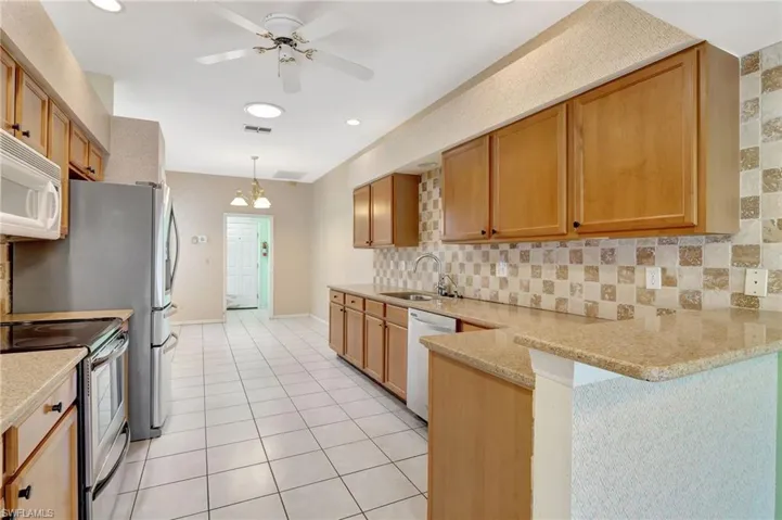Kitchen featuring white appliances, backsplash, a sink, visible vents, and a peninsula