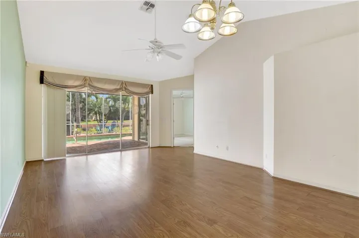 Spare room with lofted ceiling, ceiling fan with notable chandelier, baseboards, visible vents, and wood finished floors