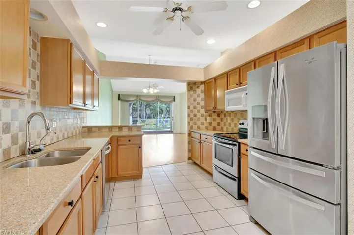 Kitchen featuring light tile patterned floors, decorative backsplash, a sink, a peninsula, and appliances with stainless steel finishes