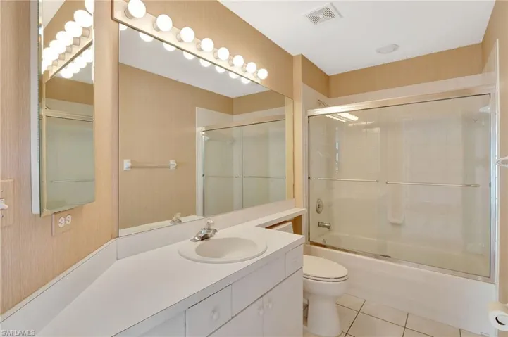 Full bathroom with tile patterned flooring, shower / bath combination with glass door, vanity, toilet, and visible vents