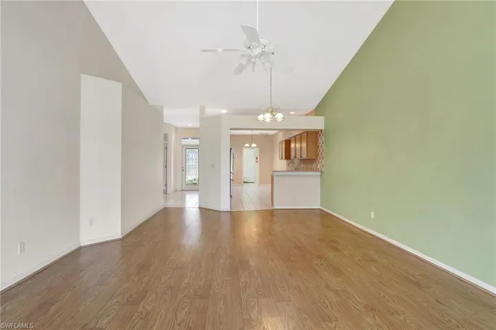 Unfurnished living room with baseboards, high vaulted ceiling, ceiling fan with notable chandelier, and light wood finished floors