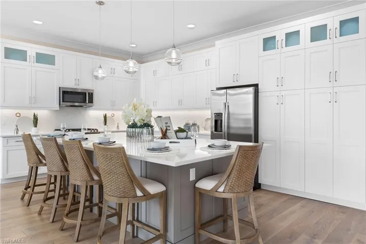 Kitchen with a kitchen bar, stainless steel appliances, decorative light fixtures, white cabinetry, and an island with sink