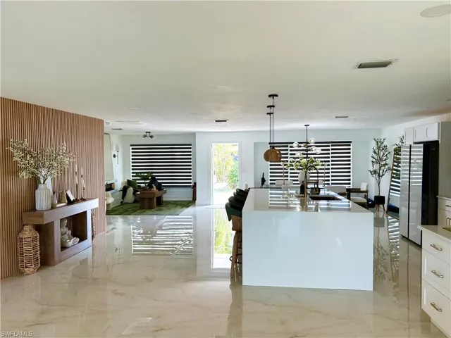 Kitchen with white cabinetry, freestanding refrigerator, hanging light fixtures, a center island with sink, and a breakfast bar area