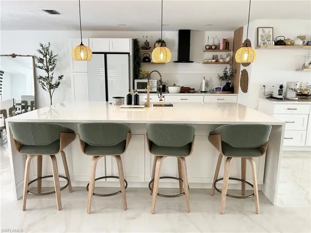 Kitchen with white cabinetry, a large island with sink, hanging light fixtures, and a breakfast bar