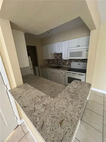 Kitchen with light tile patterned floors, white appliances, a textured ceiling, backsplash, and light stone countertops