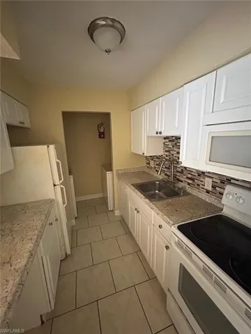 Kitchen with white appliances, white cabinetry, decorative backsplash, and light tile patterned floors