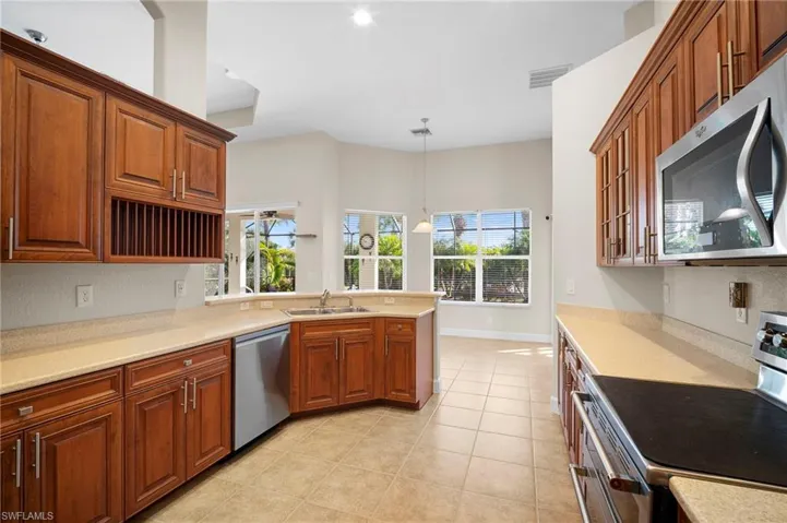 Kitchen with appliances with stainless steel finishes, decorative light fixtures, a peninsula, and brown cabinets
