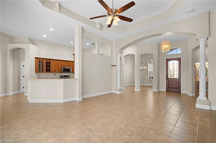 Entrance foyer with arched walkways, a towering ceiling, a chandelier, light tile patterned floors, and a ceiling fan