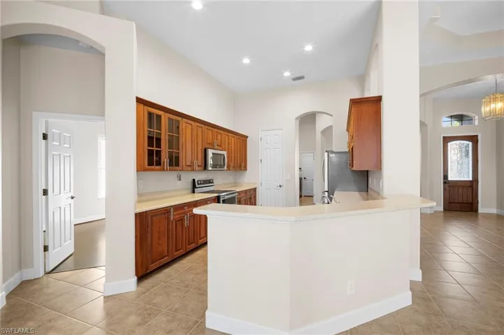Kitchen featuring brown cabinets, arched walkways, a peninsula, stainless steel appliances, and light tile patterned flooring
