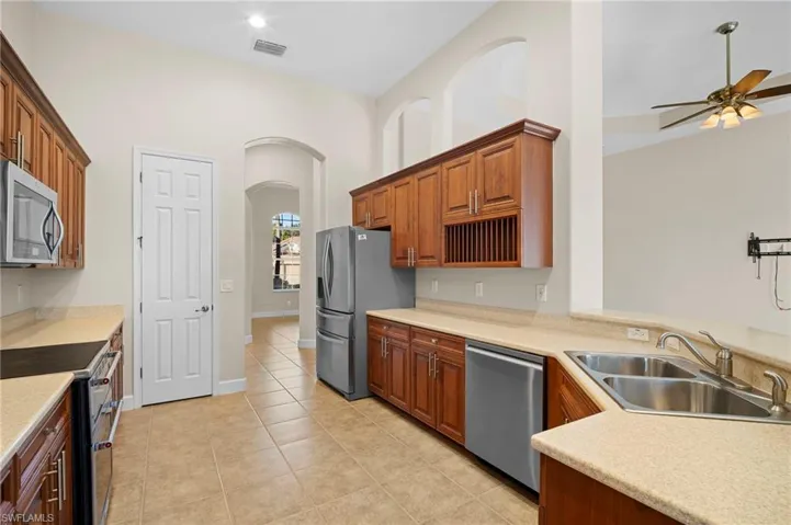 Kitchen featuring stainless steel appliances, light tile patterned flooring, brown cabinetry, a ceiling fan, and arched walkways